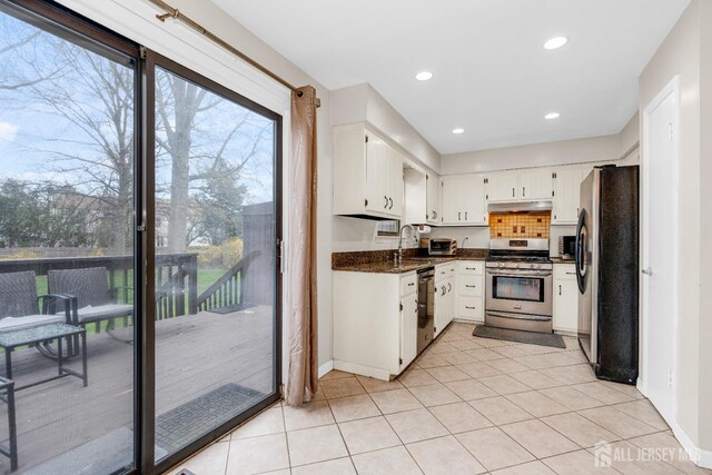 kitchen featuring baseboards, light tile patterned floors, stainless steel appliances, under cabinet range hood, and white cabinetry