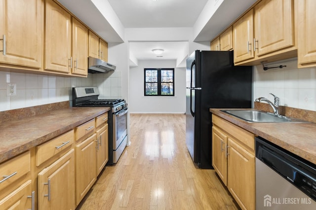 kitchen with dark countertops, stainless steel appliances, a sink, light wood finished floors, and under cabinet range hood