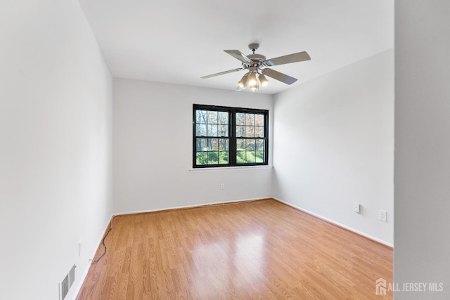 empty room featuring a ceiling fan, visible vents, light wood-style floors, and baseboards