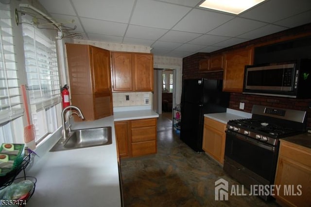 kitchen featuring appliances with stainless steel finishes, a sink, a drop ceiling, brown cabinetry, and light countertops