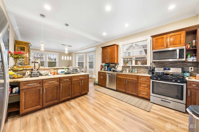 kitchen with pendant lighting, light hardwood / wood-style flooring, appliances with stainless steel finishes, sink, and backsplash