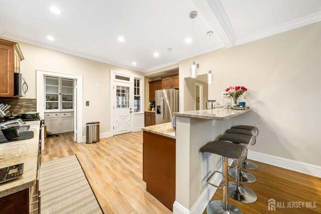 kitchen with pendant lighting, stainless steel appliances, a kitchen breakfast bar, kitchen peninsula, and light stone counters