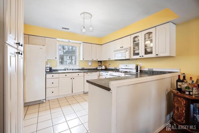 kitchen featuring a sink, dark countertops, white appliances, a peninsula, and light tile patterned floors