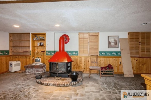 57 Jensen St, East Brunswick, NJ 08816 - living room with a wood stove, wood walls, a textured ceiling, wainscoting, and stone finish flooring