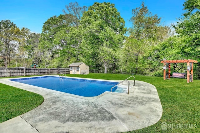 view of pool with a patio area, an outbuilding, view of wooded area, and a playground