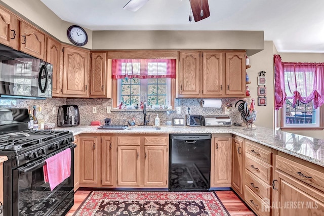 kitchen featuring black appliances, a sink, light wood-style floors, tasteful backsplash, and light stone counters