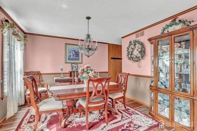 dining room with a chandelier, light wood finished floors, healthy amount of natural light, ornamental molding, and baseboards