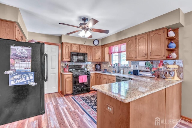 kitchen with black appliances, a peninsula, a sink, ceiling fan, and light wood-style flooring