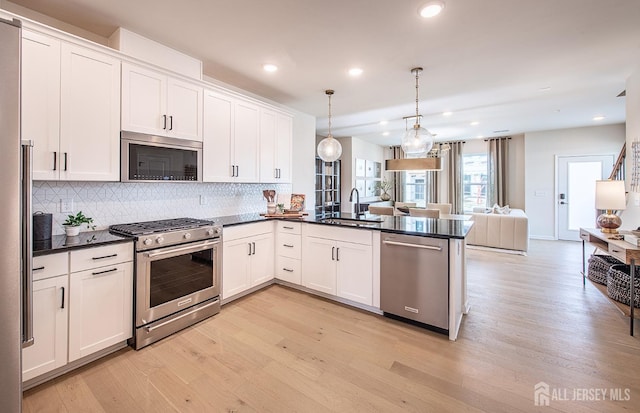 kitchen featuring dark countertops, open floor plan, appliances with stainless steel finishes, a peninsula, and a sink