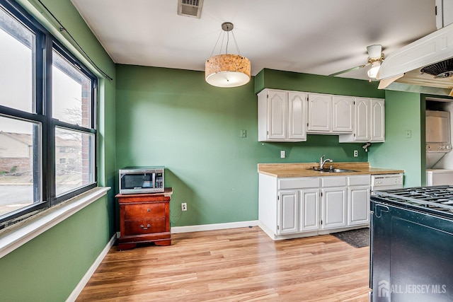 kitchen with pendant lighting, white cabinets, sink, stacked washing maching and dryer, and ceiling fan