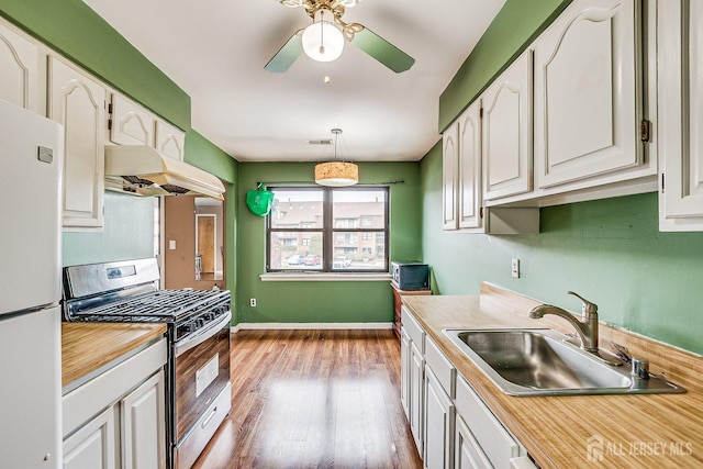 kitchen with stainless steel range with gas cooktop, white refrigerator, pendant lighting, white cabinets, and sink