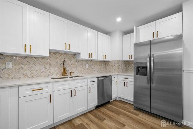 kitchen featuring tasteful backsplash, sink, white cabinets, stainless steel appliances, and light wood-type flooring