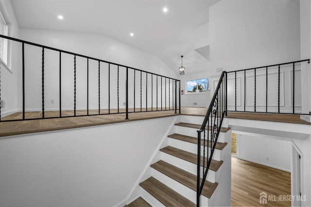 staircase with lofted ceiling, a notable chandelier, and hardwood / wood-style flooring