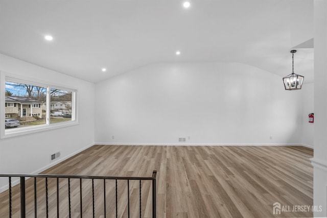 spare room featuring a notable chandelier, vaulted ceiling, and light hardwood / wood-style floors