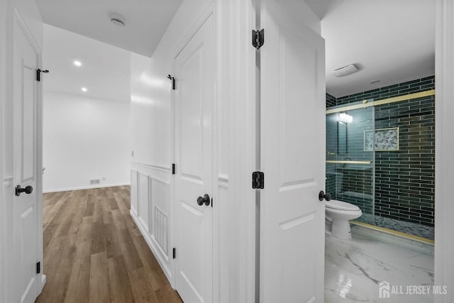 bathroom with wood-type flooring, a shower with door, and toilet