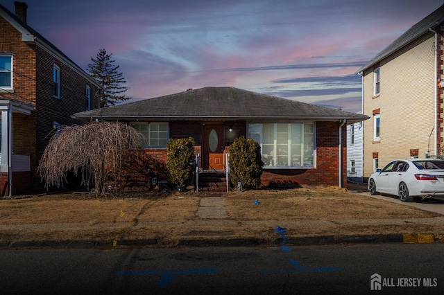 bungalow-style home with a shingled roof and brick siding