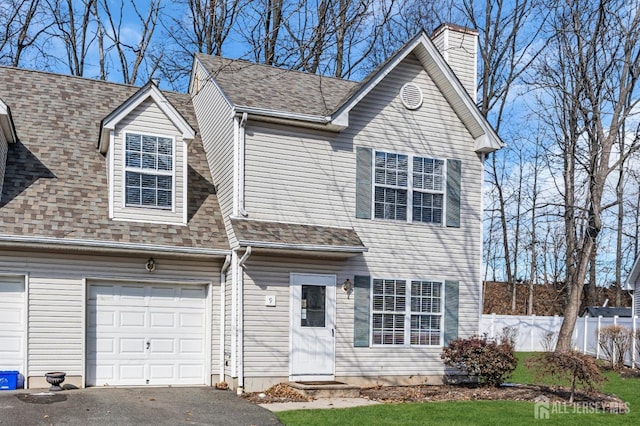 view of front facade featuring a garage, a shingled roof, a chimney, aphalt driveway, and fence