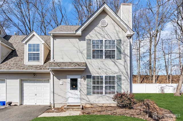 view of front facade with aphalt driveway, an attached garage, fence, a front lawn, and a chimney