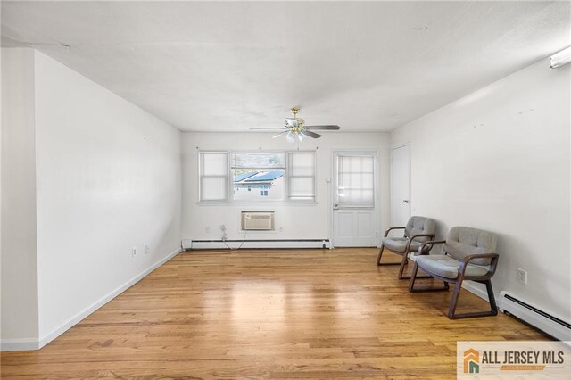 sitting room with a baseboard heating unit, baseboards, light wood-style flooring, and a ceiling fan