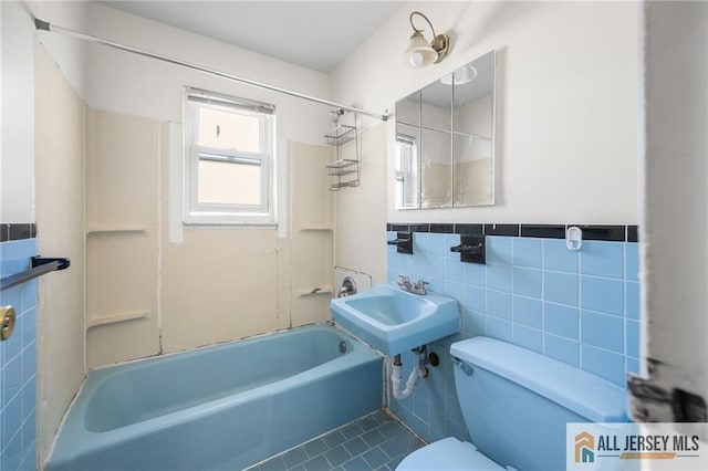 bathroom with tile walls, toilet, wainscoting, a sink, and  shower combination