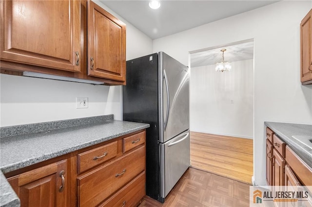 kitchen featuring brown cabinetry, decorative light fixtures, freestanding refrigerator, parquet flooring, and a notable chandelier