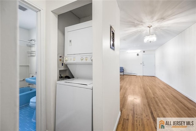 clothes washing area featuring laundry area, visible vents, wood finished floors, stacked washing maching and dryer, and a baseboard heating unit