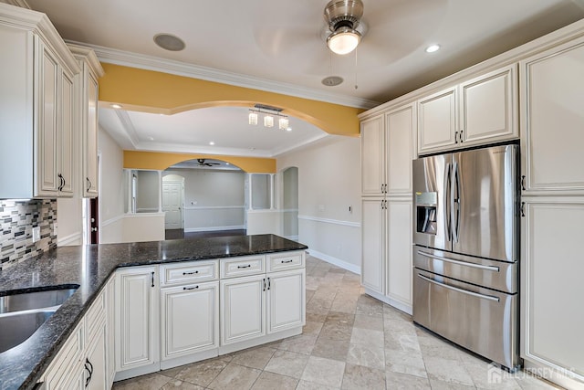 kitchen featuring stainless steel fridge, arched walkways, a peninsula, crown molding, and backsplash