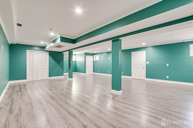 basement featuring light wood finished floors, baseboards, visible vents, and crown molding