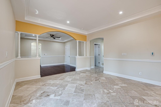 empty room with arched walkways, a ceiling fan, baseboards, ornamental molding, and a raised ceiling