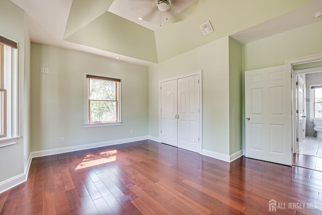 unfurnished bedroom featuring baseboards, multiple windows, visible vents, and dark wood-type flooring