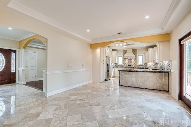 kitchen featuring arched walkways, a sink, custom exhaust hood, stainless steel fridge with ice dispenser, and tasteful backsplash