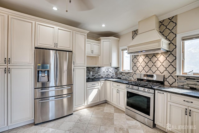 kitchen with plenty of natural light, custom range hood, appliances with stainless steel finishes, and backsplash