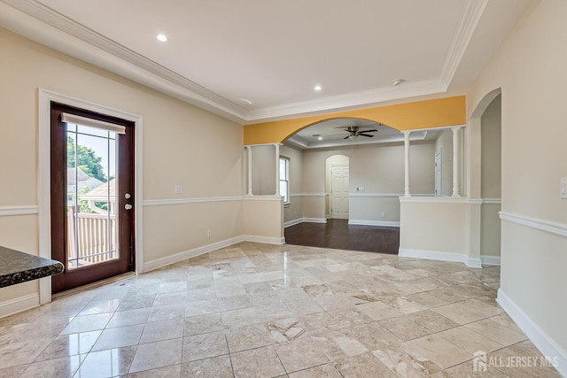 unfurnished room with ornamental molding, arched walkways, a tray ceiling, and baseboards