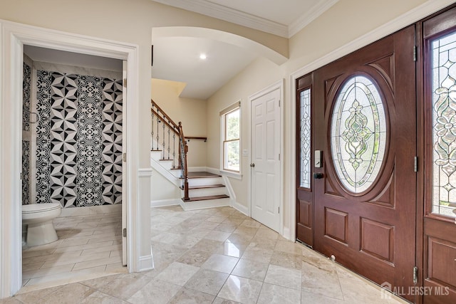 foyer entrance featuring ornamental molding, arched walkways, stairway, and baseboards