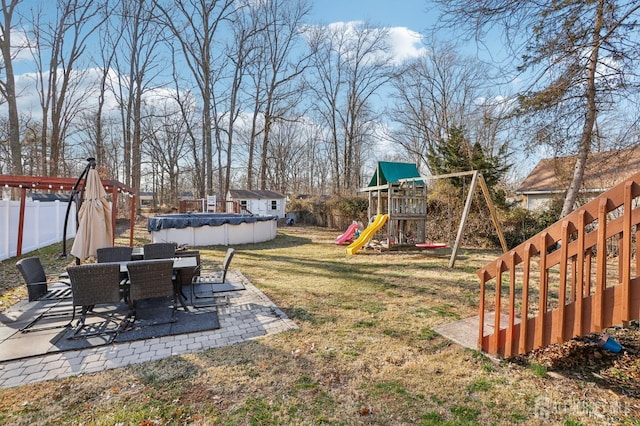 view of yard with outdoor dining space, a patio, fence, a covered pool, and a playground