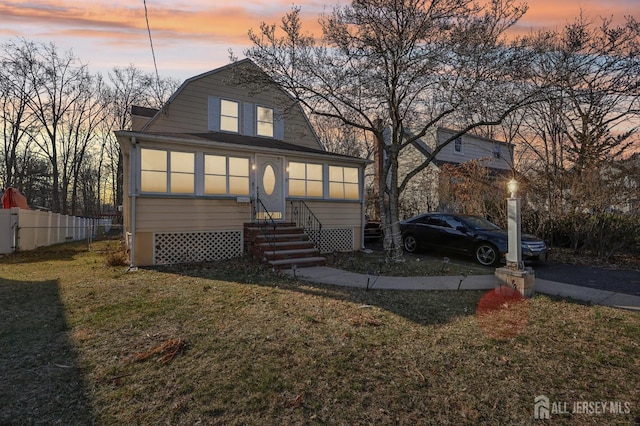 view of front facade with fence, aphalt driveway, a gambrel roof, entry steps, and a front yard