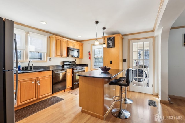 kitchen featuring a sink, black appliances, light wood-style floors, a kitchen bar, and dark countertops