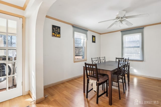 dining area featuring baseboards, arched walkways, light wood-style floors, and crown molding