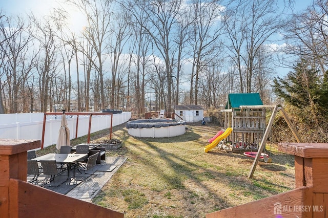 view of yard with an outbuilding, outdoor dining area, a fenced backyard, a storage shed, and a playground