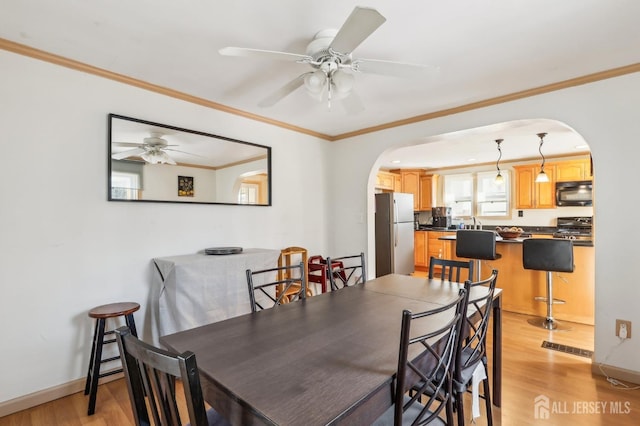 dining room with crown molding, baseboards, light wood-style flooring, arched walkways, and a ceiling fan