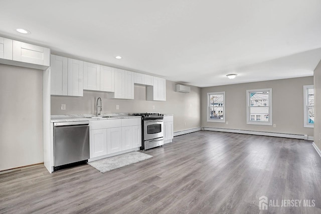 kitchen with a wall unit AC, stainless steel appliances, light countertops, a baseboard heating unit, and white cabinets