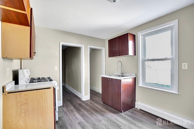 kitchen featuring a baseboard heating unit, wood finished floors, a sink, light countertops, and gas range oven