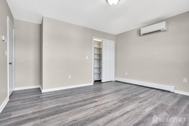 unfurnished bedroom featuring baseboards, a baseboard heating unit, wood finished floors, and a wall mounted air conditioner