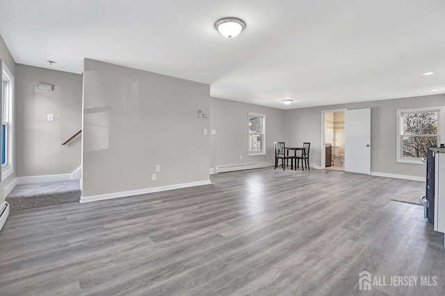 unfurnished living room featuring a baseboard radiator, wood finished floors, and baseboards