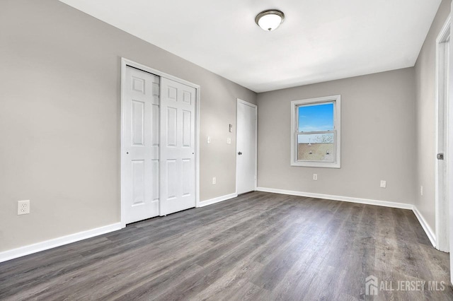 unfurnished bedroom featuring a closet, dark wood finished floors, and baseboards