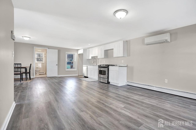 kitchen featuring a baseboard radiator, appliances with stainless steel finishes, wood finished floors, an AC wall unit, and white cabinetry