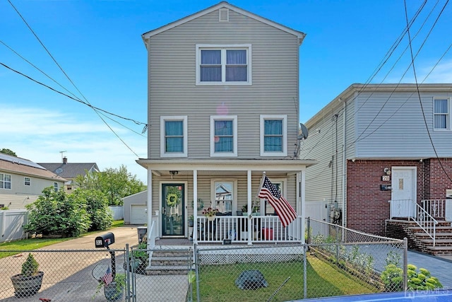 traditional-style house featuring a fenced front yard, a detached garage, covered porch, driveway, and a front lawn