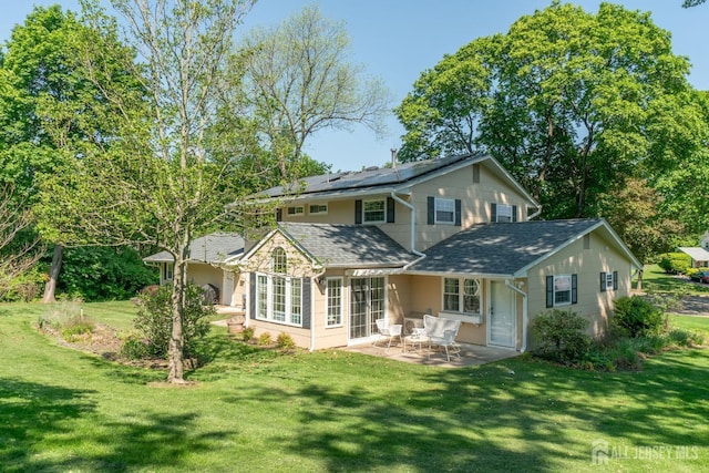 rear view of property with roof mounted solar panels, a patio area, a lawn, and roof with shingles