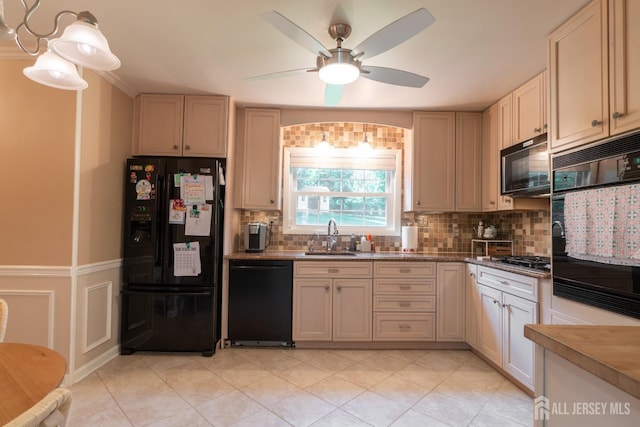 kitchen with black appliances, a sink, a ceiling fan, decorative backsplash, and a wainscoted wall