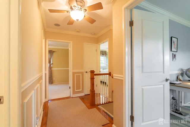 hall with an upstairs landing, ornamental molding, wood finished floors, and a decorative wall